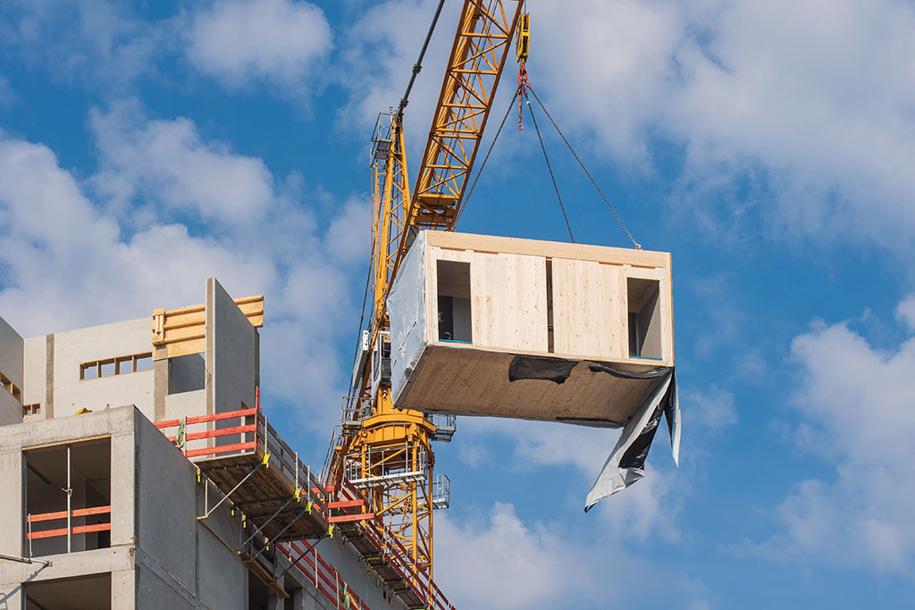 Crane lifting a wooden building module to its position in the structure. Construction site of an office building in Berlin. The new structure will be built in modular timber construction.